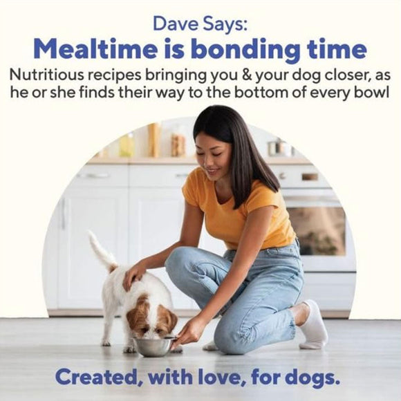 Woman in yellow shirt and blue jeans feeding a dog from a bowl on a kitchen floor.